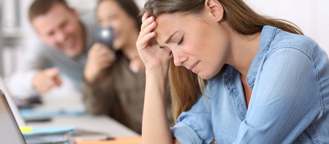 Sad cyber bullying victim being photographed by her colleagues at office